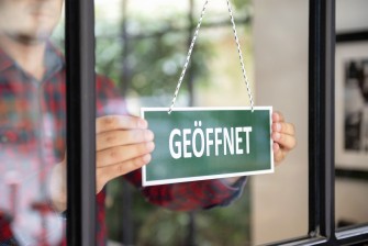 
An einem Fenster hängt ein grünes Schild mit der Aufschrift "Geöffnet".